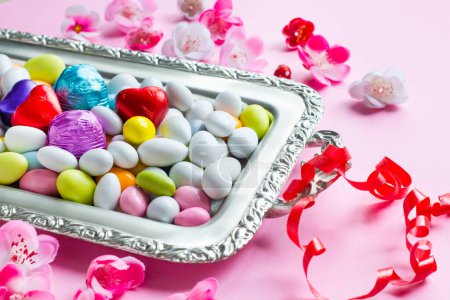 Bonbons aux amandes colorées et plateau argenté chocolat conçu avec des fleurs de printemps sur la surface rose