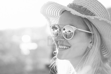 Photo for A blonde girl smiling with hat on - Beach and sunlight reflected in sunglasses - Beautiful young women in holidays - Portrait photo - Royalty Free Image