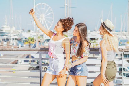 Téléchargez les photos : Groupe de filles prenant selfie pendant les vacances avec un terrain de jeu de plage dans une journée ensoleillée et s'amuser ensemble - Amis utilisant des téléphones mobiles pour suivre whith médias sociaux - en image libre de droit