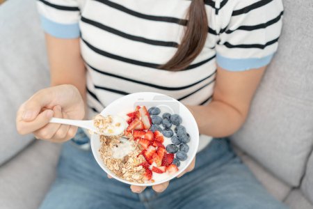 Mujer tomando delicioso desayuno saludable en casa por la mañana. Cuidado de la salud femenina come yogur con granola y fruta de bayas. Comida saludable, Vitaminas, dieta limpia, dieta, desintoxicación, comida vegetariana, orgánica.