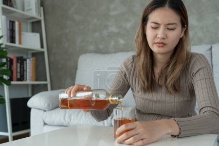 Depressed young Asian woman addicted feeling bad drinking whiskey alone at home, stressed frustrated lonely drinking alcohol suffers from problematic liquor, alcoholism, life and family problems