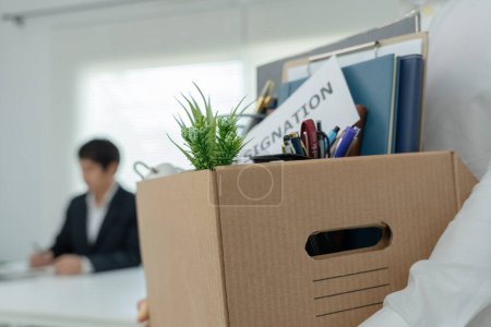 Los empresarios estresantes renunciarán a la compañía. Está levantando una caja de papel marrón que contiene objetos personales. concepto de renuncia, colocación de empleo y vacantes.
