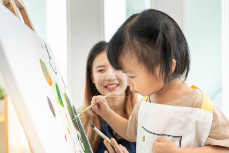Glückliche asiatische Mutter beim Malen für kleines Mädchen. Lustige Familie ist glücklich und aufgeregt im Haus. Mutter und Tochter haben Spaß dabei, Zeit miteinander zu verbringen. Urlaub, Aktivität