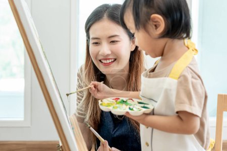 Glückliche asiatische Mutter beim Malen für kleines Mädchen. Lustige Familie ist glücklich und aufgeregt im Haus. Mutter und Tochter haben Spaß dabei, Zeit miteinander zu verbringen. Urlaub, Aktivität