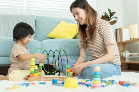 Glückliche Asia-Mutter spielt und lernt mit dem kleinen Mädchen Spielzeugklötze. Lustige Familie ist glücklich und aufgeregt im Haus. Mutter und Tochter haben Spaß dabei, Zeit miteinander zu verbringen. Urlaub, Aktivitäten, Entwicklung