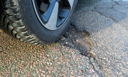 Pothole after frost on the road, symbolic with car tires