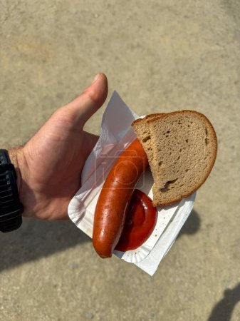 Hand hält eine Räucherwurst mit Brot und Ketchup