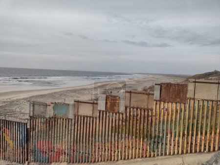 Téléchargez les photos : Vue sombre du mur protecteur de la frontière rouillée Mexique Tijuana et États-Unis d'Amérique. Défense contre l'immigration illégale, les stupéfiants, les drogues et le trafic de substances illicites en raison de l'activité du cartel. - en image libre de droit
