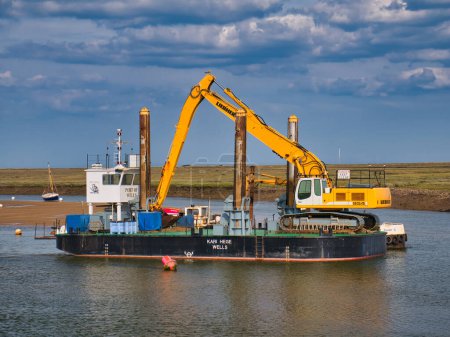 Foto de En el Puerto de Wells, Norfolk, Reino Unido, la draga portuaria Kari Hege, un pontón especialista de 20m por 10m con tecnología de monitoreo de profundidad y retroexcavadora JCB de largo alcance. - Imagen libre de derechos