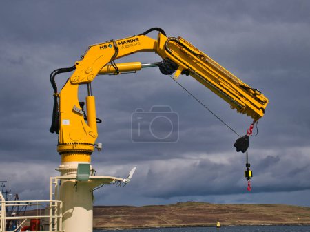 Photo for A yellow HS Marine AK 4818.5 fully foldable knuckle and telescopic boom type marine crane. Taken in sunlight with a grey sky. - Royalty Free Image
