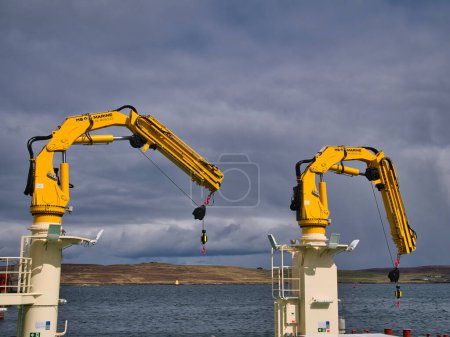 Photo for Two yellow HS Marine AK 48 18.5 fully foldable knuckle and telescopic boom type marine cranes. Taken in sunlight with a grey sky. - Royalty Free Image