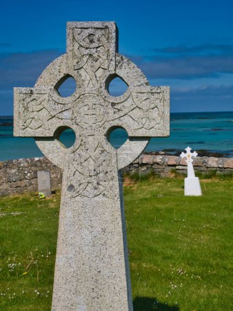 Photo for A cross in a coastal graveyard on the island of Eriskay in the Outer Hebrides, Scotland, UK. Taken on a clear, calm day in summer with a blue sky and turquoise waters. - Royalty Free Image