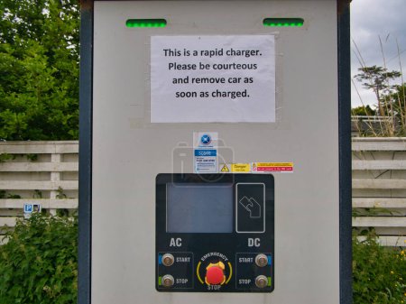 Photo for An EV (electric vehicle) rapid charger with a sign asking customers to be courteous and to move their car when charged. Taken in Tarbert, Isle of Harris in Scotland, UK. - Royalty Free Image