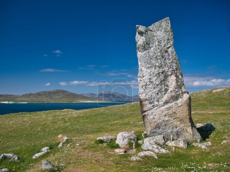 Photo for The 3m high MacLeod's Stone on the machair on the Atlantic coast of the Isle of Harris in the Outer Hebrides, Scotland, UK. The island of Taransay can be seen behind. - Royalty Free Image