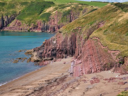 Foto de Acantilados rojos costeros cerca de Manorbier en Pembrokeshire, Gales, Reino Unido - los estratos rocosos verticalmente inclinados del lecho rocoso son del Grupo Milford Haven - rocas areniscas y areniscas, intercaladas. - Imagen libre de derechos