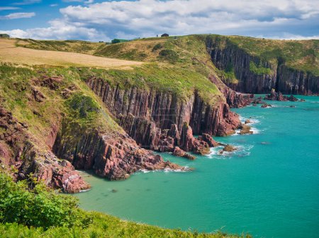 Foto de Acantilados rojos costeros cerca de Manorbier en Pembrokeshire, Gales, Reino Unido - los estratos rocosos verticalmente inclinados del lecho rocoso son del Grupo Milford Haven - rocas areniscas y areniscas, intercaladas. - Imagen libre de derechos