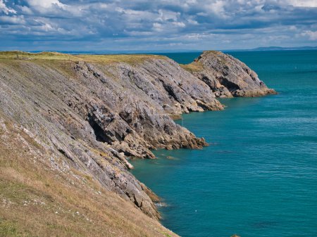 Foto de Acantilados costeros cerca de Giltar Point en Pembrokeshire, Gales, Reino Unido - los estratos rocosos inclinados de la roca caliza son del Grupo de Caliza Pembroke. Tomada en un día soleado con un mar tranquilo y azul. - Imagen libre de derechos