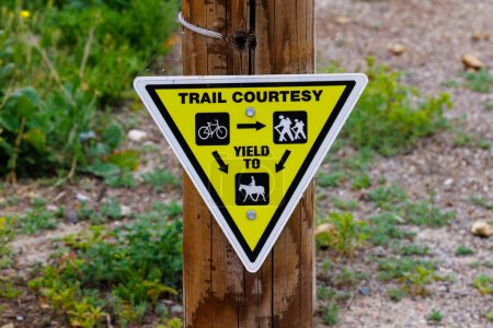 Foto de Señal de cortesía de sendero amarillo triangular en un poste de madera dando instrucciones de rendimiento - Imagen libre de derechos