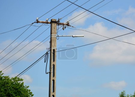 Strommast mit Kabeln und Lampe gegen blauen Himmel