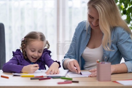 Foto de Enseñando arte infantil y dibujo en casa. Joven madre enseñar a la pequeña hija a pintar con lápices de colores y lápices de colores en papel disfrutando de un tiempo feliz juntos - Imagen libre de derechos