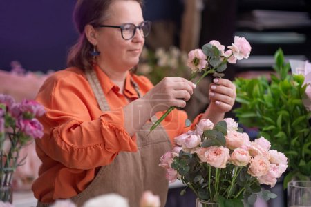 Téléchargez les photos : Femme décorateur de fleurs concepteur floral travaillant sur ordinateur portable au studio de magasin de douche. bouquets autour, entreprise de fleurs - en image libre de droit