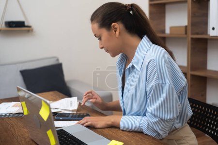 woman accountant, committed to bookkeeping in her home. examining annual financial reports, calculating tax rates on her calculator, and responsibly declaring freelance income
