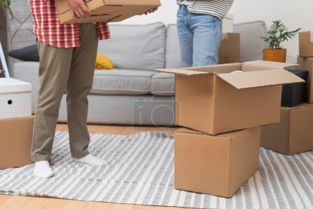 couple stands in their new homes living room, surrounded by a stack of cardboard boxes from their relocation abroad, satisfied with their move