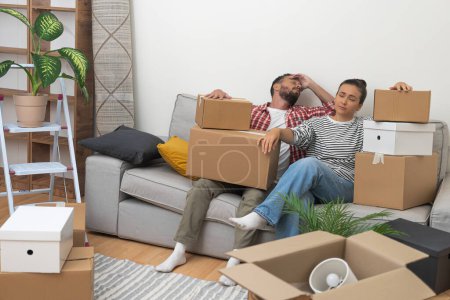 Photo for Tired man and woman relaxing on sofa after carrying packed boxes with decorative elements for new flat transforming new apartment and purchasing modern property together - Royalty Free Image