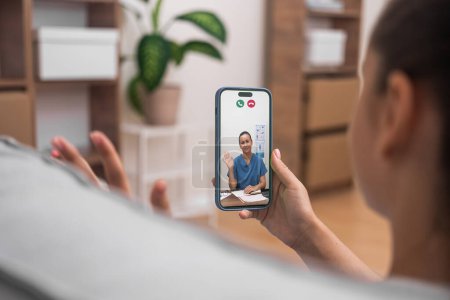 Téléchargez les photos : Consultation médicale virtuelle avec un médecin amical accueillant le patient via smartphone. - en image libre de droit