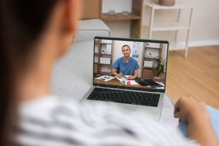 A view from behind a patient engaged in a telemedicine session with a doctor on a laptop, highlighting digital healthcare.