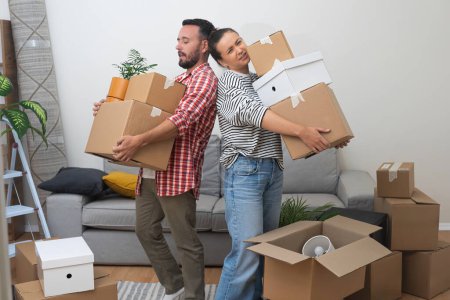 Overstressed couple of man and woman hold heavy boxes with goods delivered to new apartment cardboard packages stacked on floor in living room of accommodation
