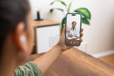 Téléchargez les photos : Télémédecine en action avec une femme médecin saluant un patient par un appel vidéo smartphone à la maison. - en image libre de droit