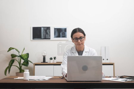 Online Health Expert: With unwavering focus, a female doctor employs her laptop to provide medical support and conduct video consultations, embodying the heart of telemedicine. 