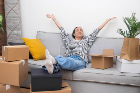 Young woman sits comfortably on sofa in cozy apartment thinking with positive about completed stage of moving to house equipped with currents technologies