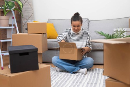 Moving Forward: Junge Frau in neuem Zuhause, umgeben von Kartons, packt ihre Welt aus und steht für Umzug, Vermietung oder Eigenheim