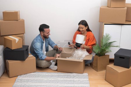 Lächelndes Paar genießt einen gemütlichen Moment beim Auspacken von Kartons in ihrer neuen Wohnung. Gemeinsam ein Leben aufbauen, Tagesglück bewegen