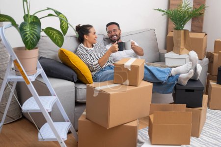 Unpacking and moving day become a celebration as a young couple cheers with coffee cups on the sofa, surrounded by boxes, making their new house their own