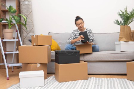 mujer joven abraza la emoción de trasladar el día desempacando sus pertenencias en el sofá en su nuevo hogar, subrayando los conceptos de reubicación y bienes raíces