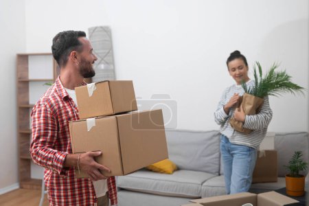 joyful couple moves to their new home, standing in the living room with a stack of cardboard boxes from their relocation service, radiating satisfaction