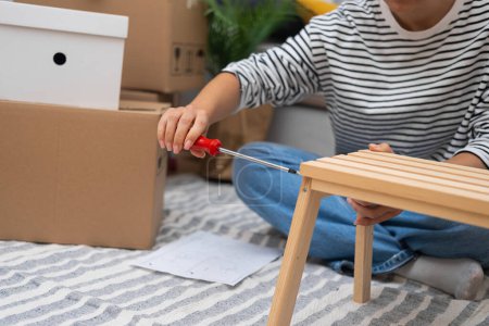 close up woman assembles a modern wooden shelf with ease, using basic tools to enhance her new living space after moving