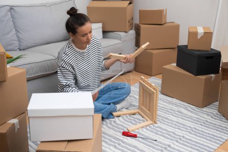 woman assembles self-assembly shelf in her new house, amidst moving carton boxes and furniture, embracing the concept of renting