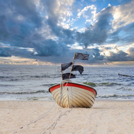 Un bateau de pêche échoué sur une plage de sable avec la mer et un ciel nuageux en arrière-plan.