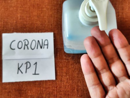Picture of an individual using hand sanitizer with CORONA KP 1 written on a placard shot against colored background. Corona virus new strain. Covid-19 Infection