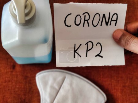 Photo d'un individu tenant une plaque avec CORONA KP 2 écrit dessus avec un désinfectant et un masque conservé sur la table. Virus Corona nouvelle souche. Infection à Covid-19