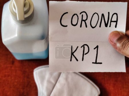 Picture of an individual holding a placard with CORONA KP 1 written on it with a sanitizer and a mask kept on table. Corona virus new strain. Covid-19 Infection