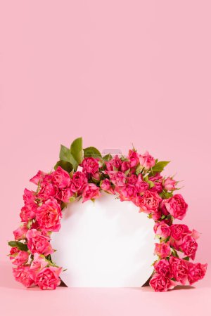 Bright fresh tiny spray roses as tender floral framing of white round arch on abstract white scene mockup for presentation cosmetic products, goods, advertising, design, vertical, copy space. 
