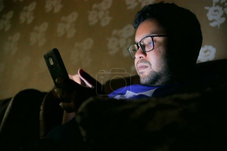 Téléchargez les photos : Jeunes hommes assis sur le canapé en utilisant le téléphone intelligent la nuit , - en image libre de droit