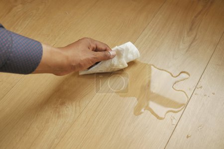 Photo for Hand wiping spilled tea with paper napkin on floor - Royalty Free Image