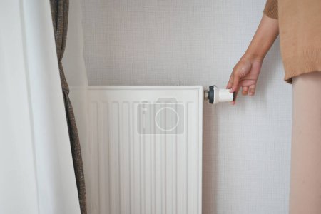 Téléchargez les photos : Les femmes tournent le bouton du radiateur.. - en image libre de droit