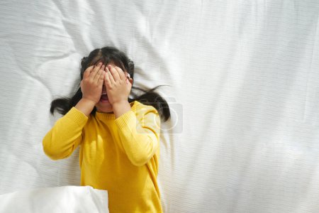 Triste enfant couvert son visage avec ses mains tout en étant couché sur le lit à la maison